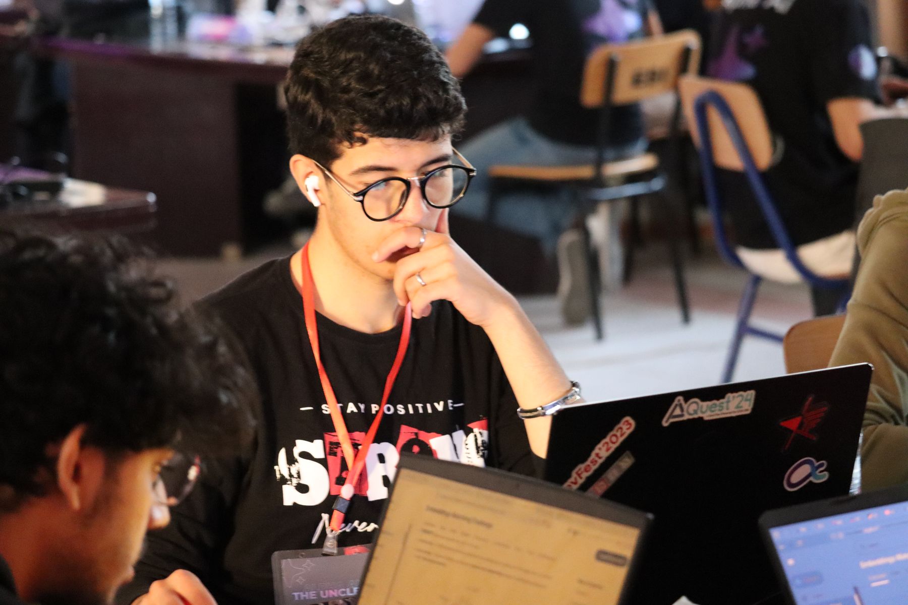 Mouadh at a hackathon table, laptop covered in AIQuest'24 and DevFest'2023 stickers
